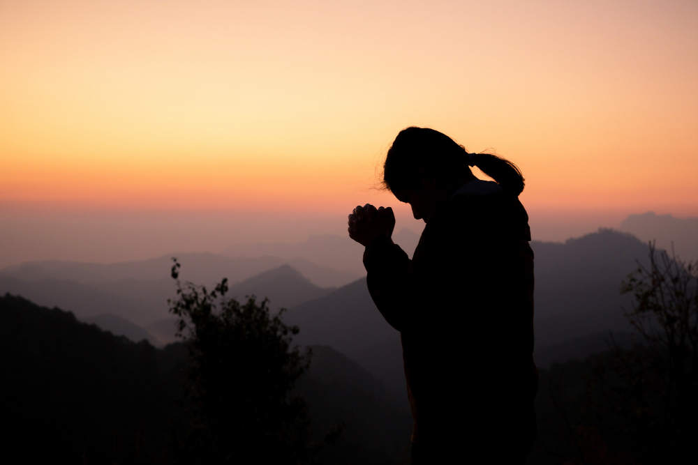 image of praying woment with sunset and mountains on the background