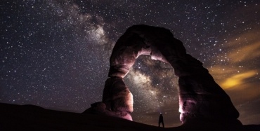 A person standing in the stone arch watching stars