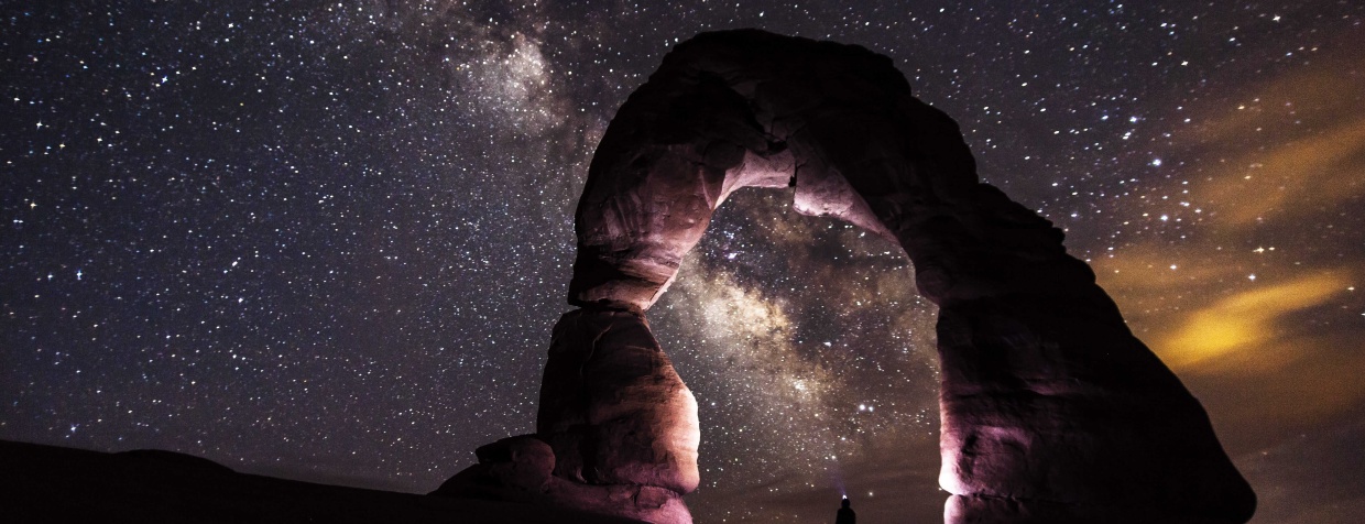 A person standing in the stone arch watching stars