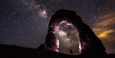 A person standing in the stone arch watching stars