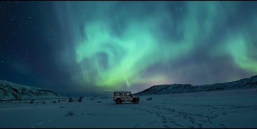 An SUV in a snowy field, against mountains and Northern Lights.