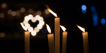 Candele accese con una luce a forma di cuore sullo sfondo.