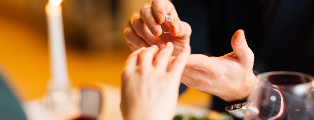 A man putting an engagement ring on a woman's finger.