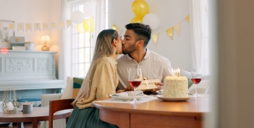 Una coppia che festeggia un compleanno a casa con torta e vino.
