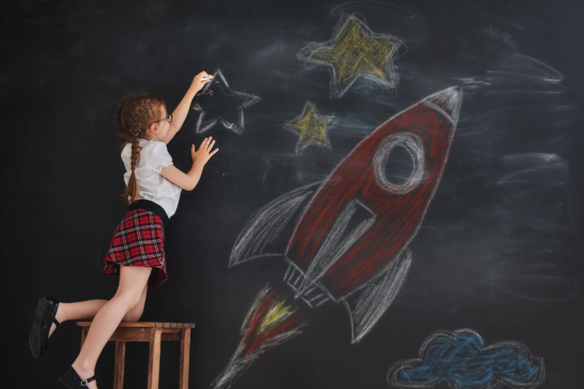 A child drawing a rocket and stars with chalk