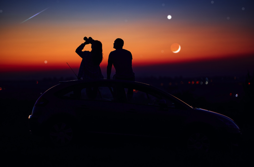 Two people sitting on a car and looking at stars with binoculars