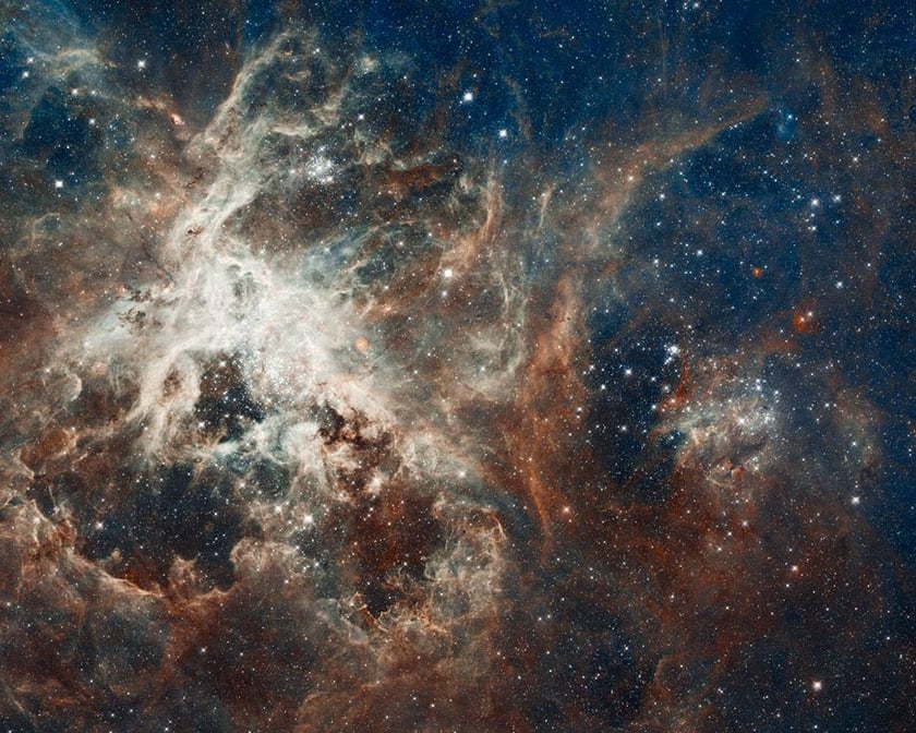 Brown, white and blue clouds of gas and dust swirling around in the cosmos full of stars