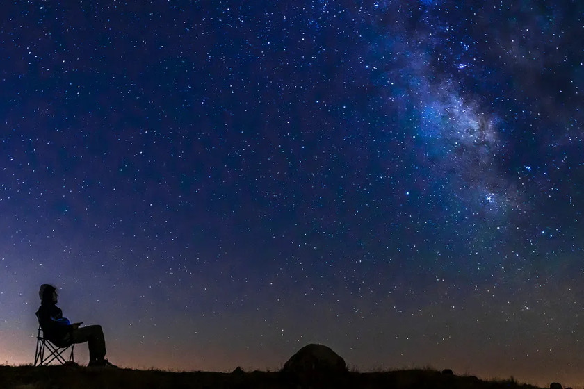 A person sittion in a chair and looking at the starry night sky