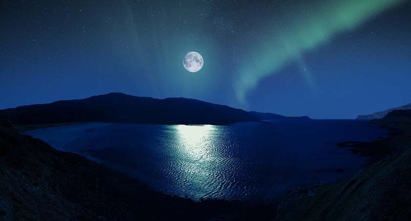 The Moon reflecting in a pond with northern lights near it