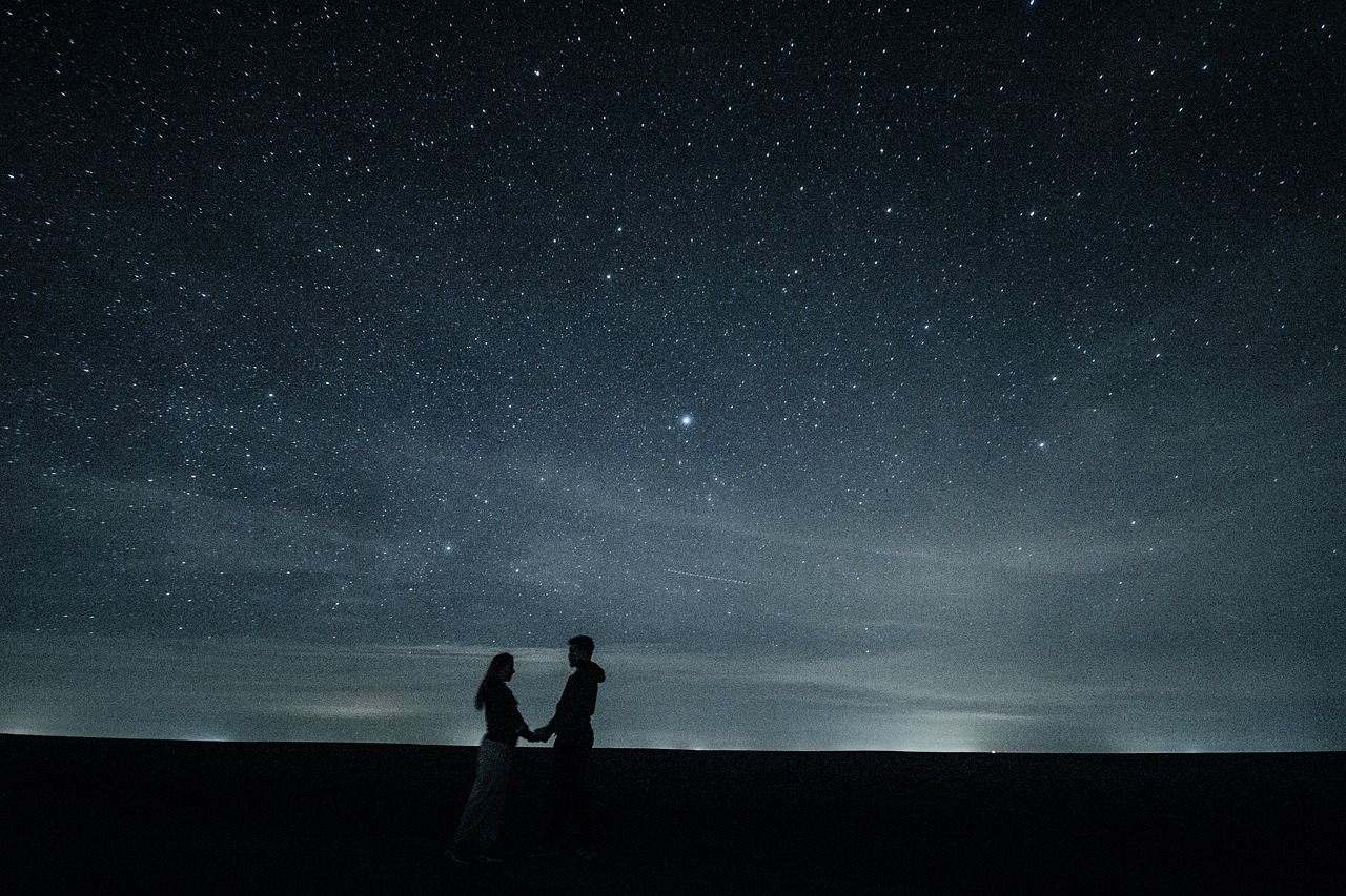 Couple holding hands under starry night sky 