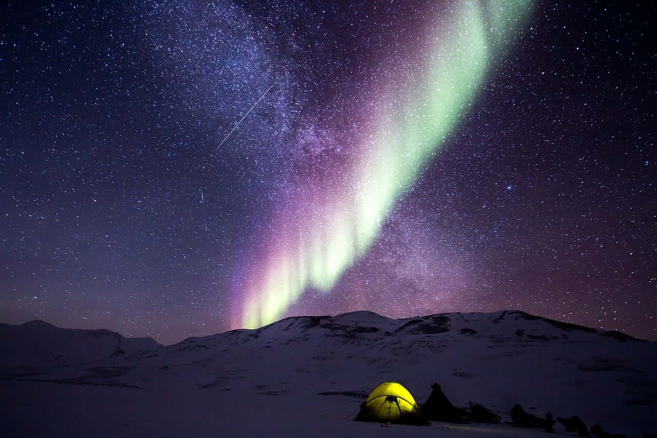 A yellow tent under colorful northern lights