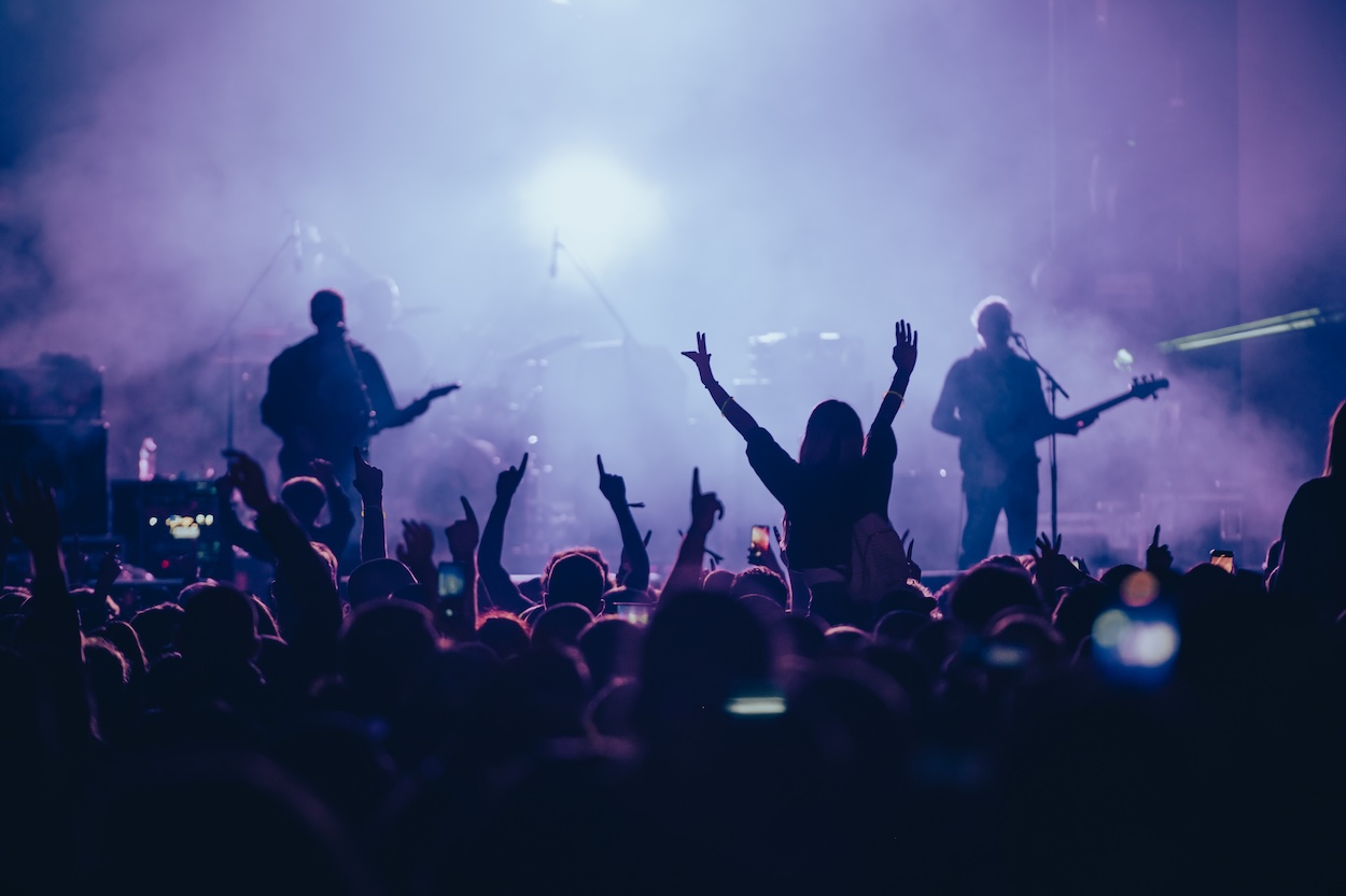 A crowd of fans cheering, and musicians performing at a concert.