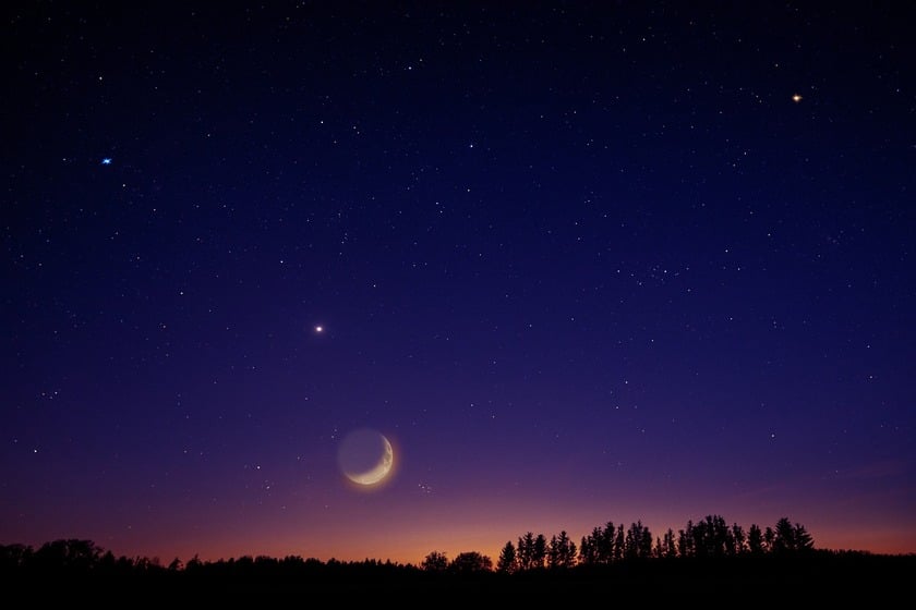 A crescent Moon shining with a lot of stars around it in the purple and orange sky