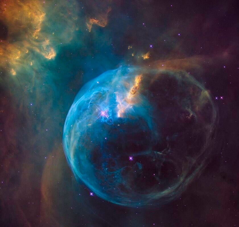 A nebula looking like a blue bubble surrounded by yellow and blue dust clouds