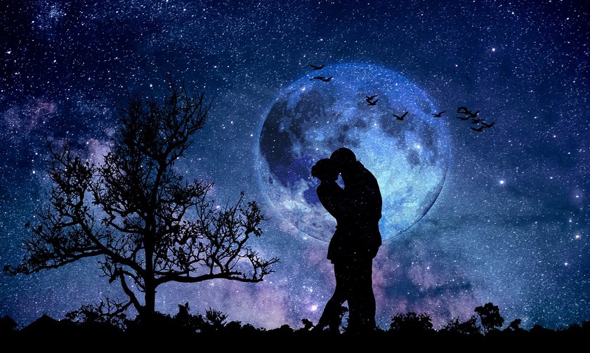 A couple kissing in front of the full Moon on a starry night by a tree