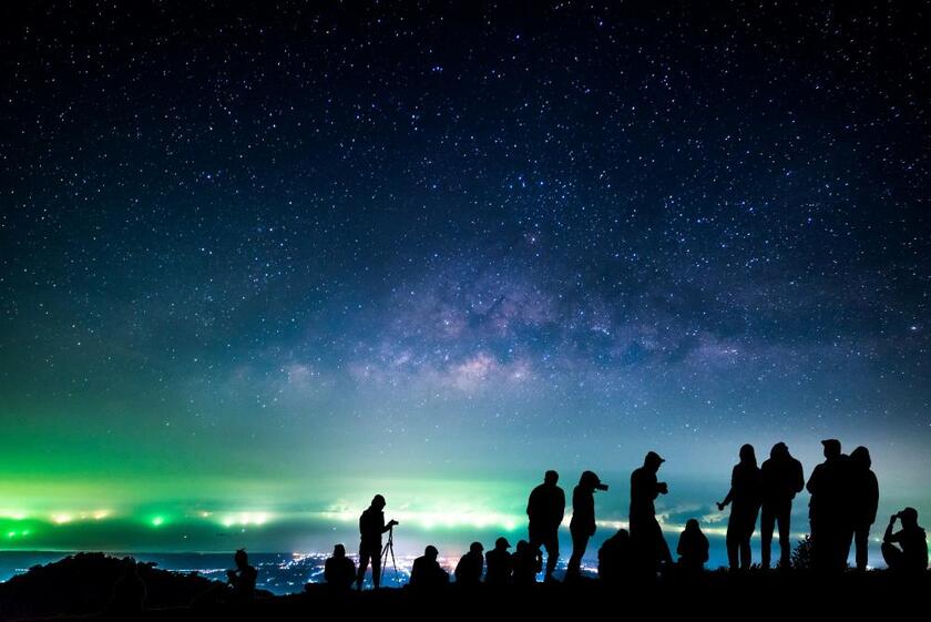 People gathered standing in the dark and looking at green and purple Northern Lights