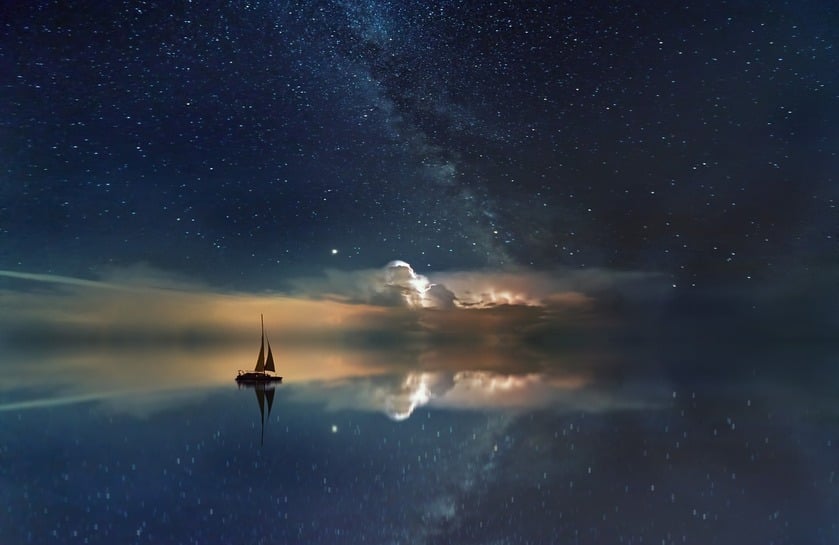 a sailboat drifting in the ocean with starry night sky above and reflecting in the water