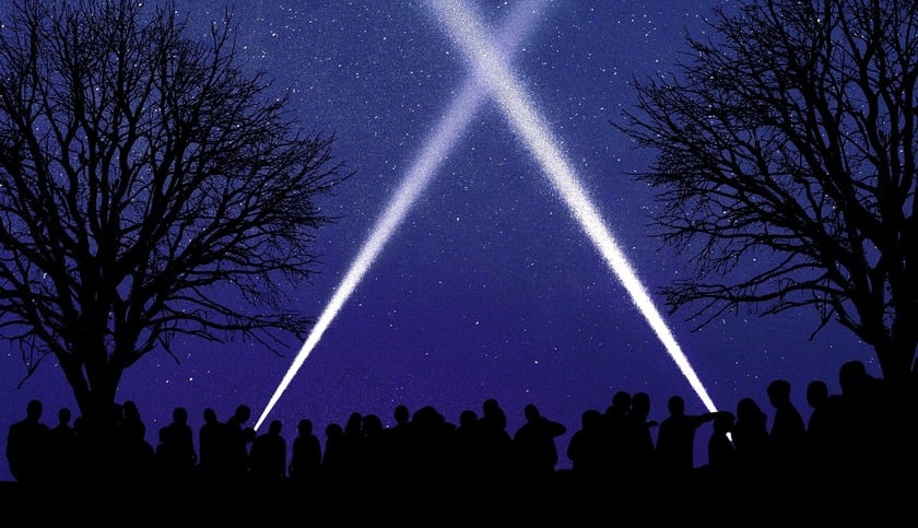 A group of people standing and pointing flashlights in the night sky near trees