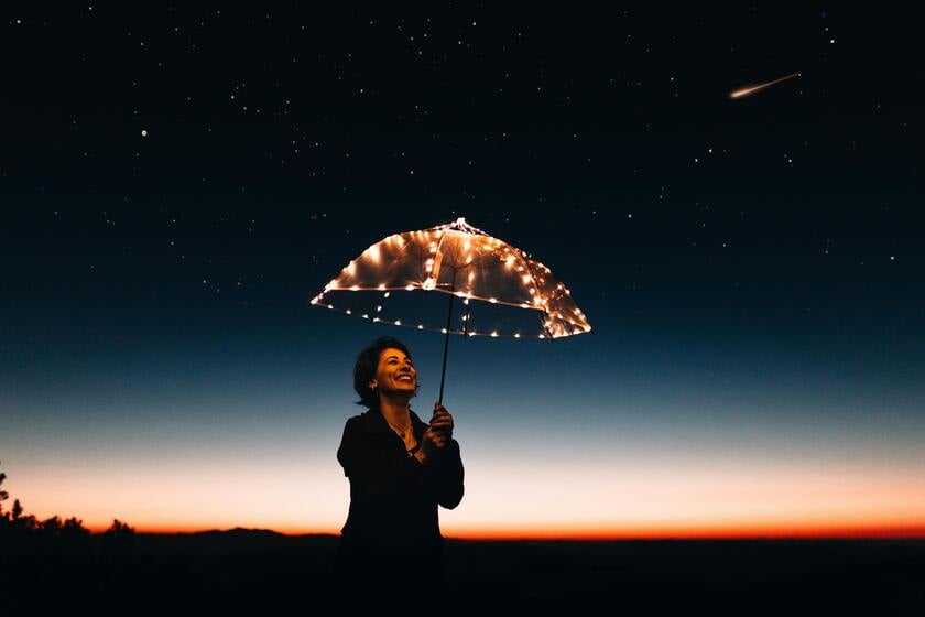 A woman standing under a sky full of stars holding a glowing umbrella