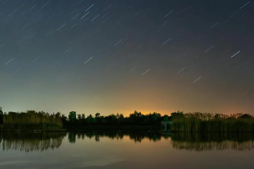 A meteor shower in a twilight above a forest line and a lake