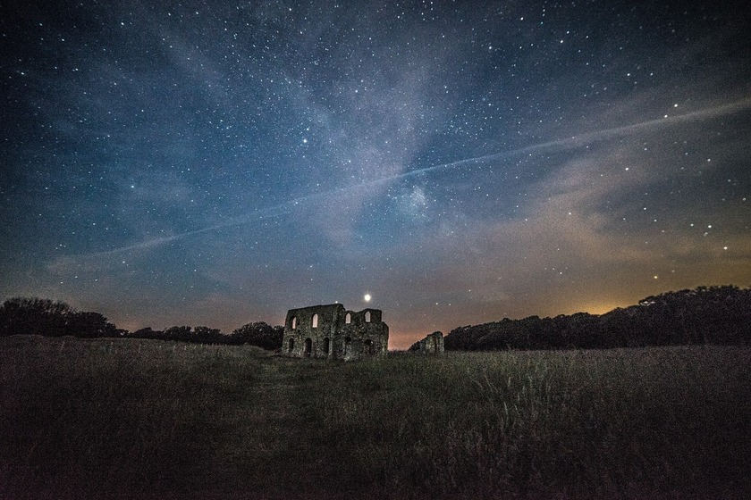 Ruins of a building in the middle of a field, night sky full of stars above it