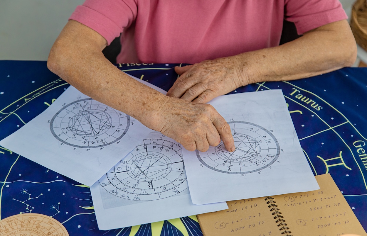 Eine &auml;ltere Person liest astrologische Karten an einem Tisch.