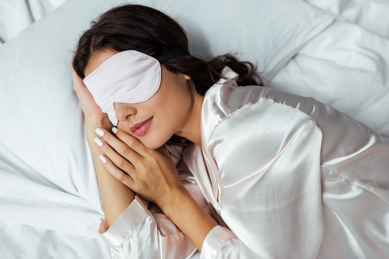 Una mujer joven durmiendo con un antifaz de seda para dormir.