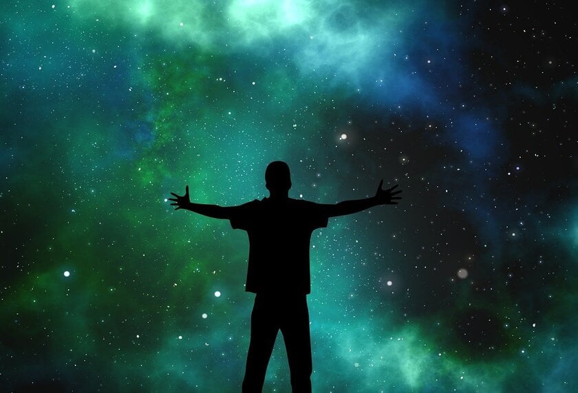 A person looking at the green and blue sky full of stars with his arms spread out