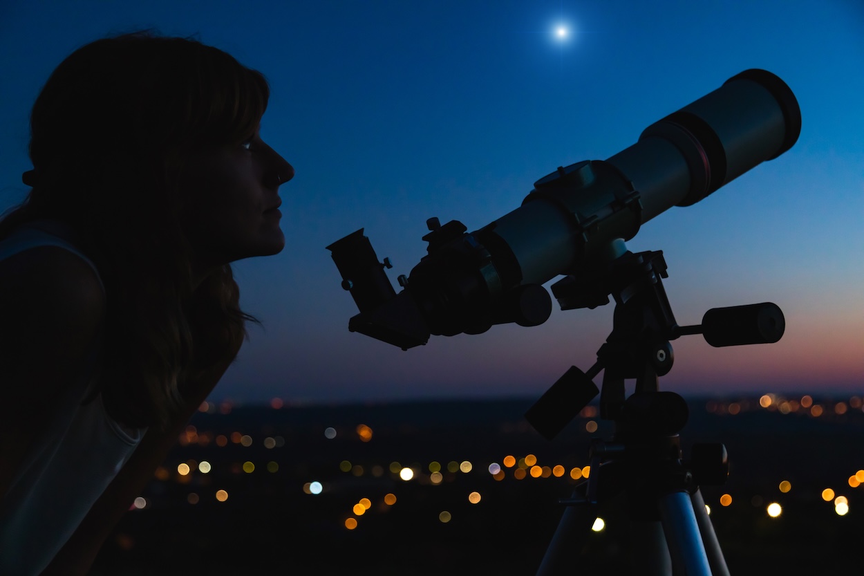 A woman stargazing near a city.