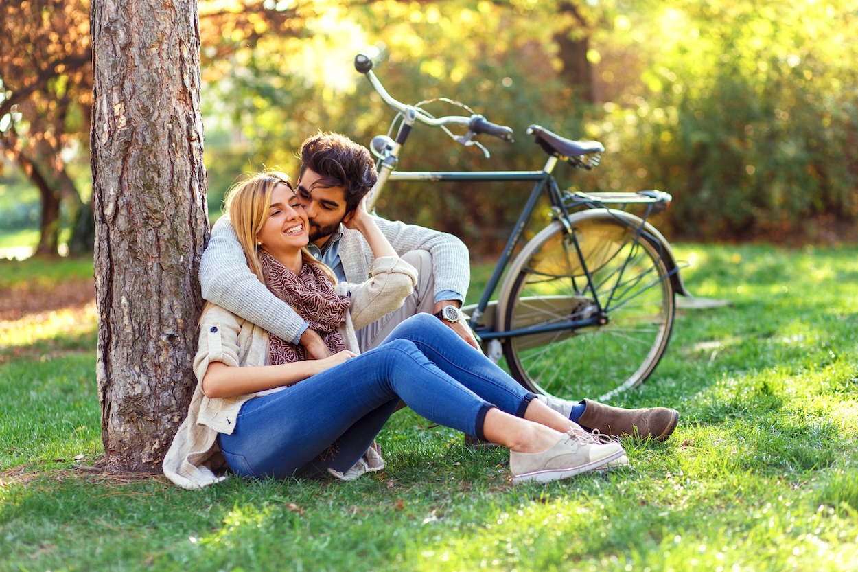 A smiling happy sitting in a park by a bicycle.