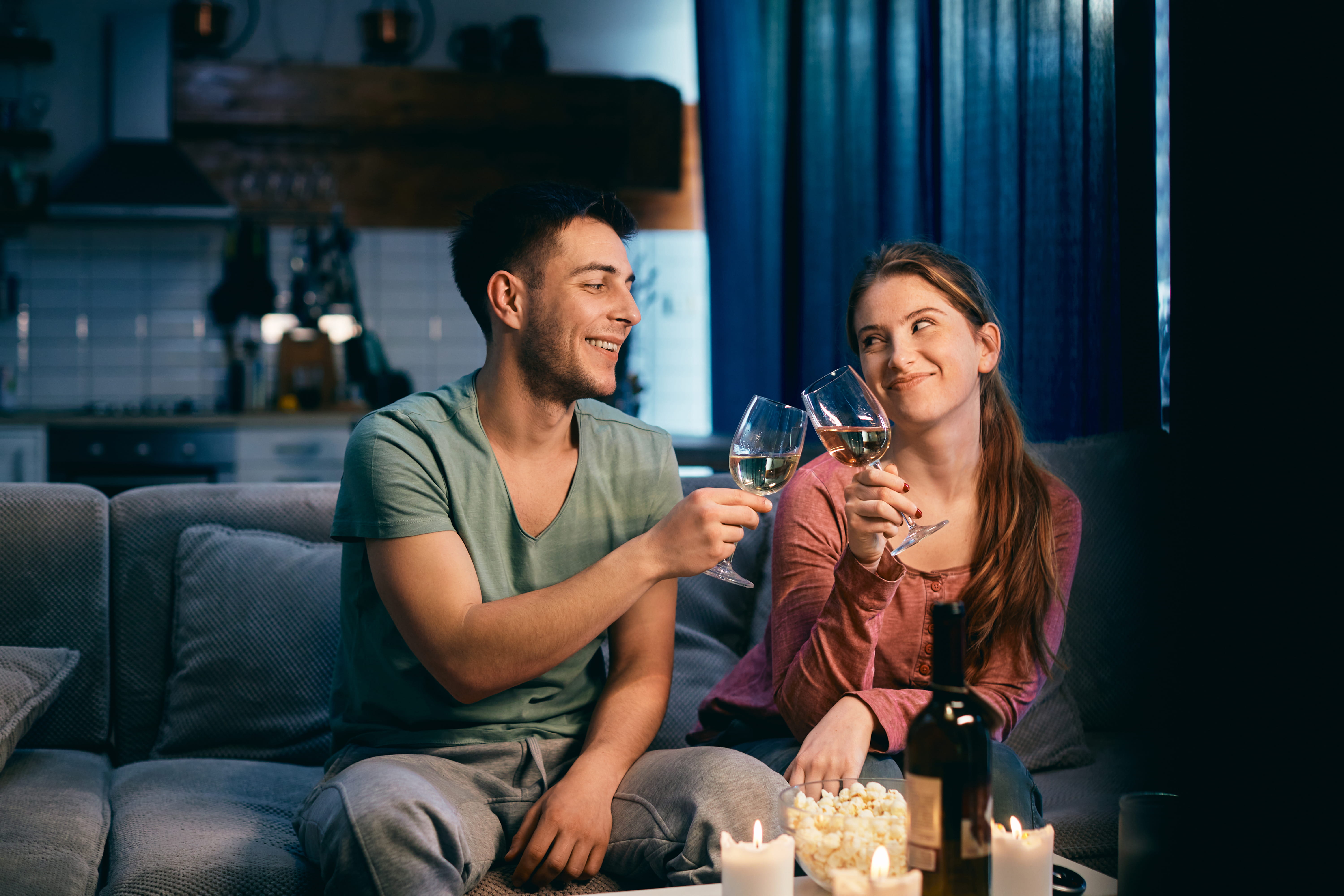 A young happy couple toasting with wine in the evening at home.